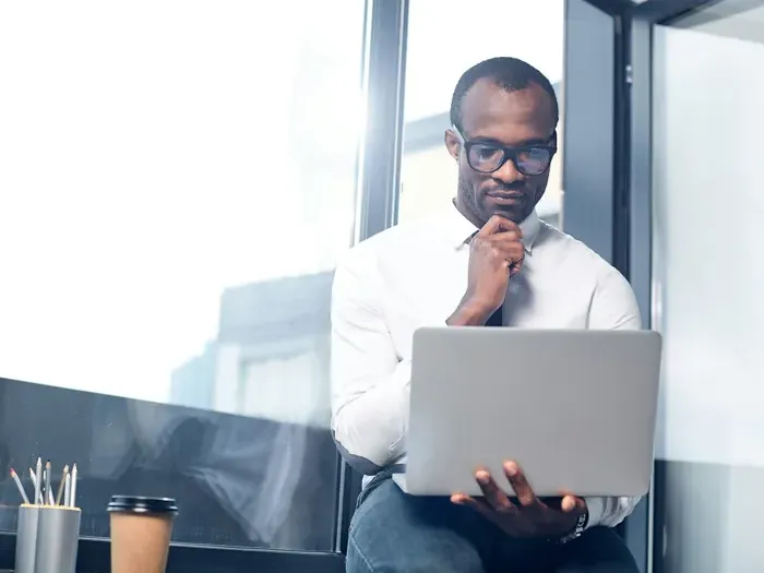 Professional with laptop by a window over the city skyline, City Service Listing Now supports entrepreneurs managing listings